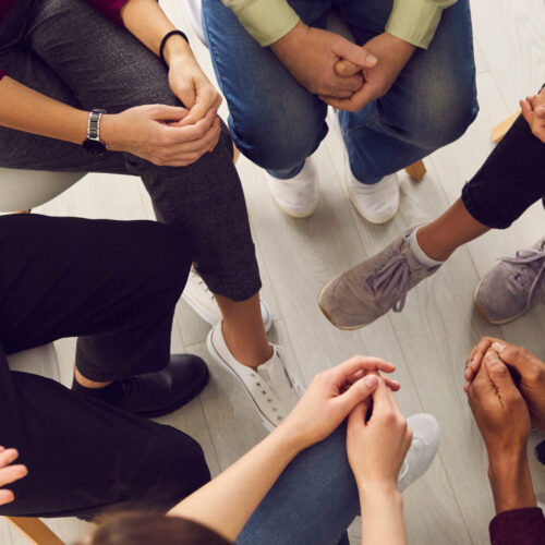 Top view of diverse people sitting in a close circle and talking to a therapist. Top view of diverse people sitting in a close circle and talking to a therapist. Cropped image of unidentified people receive help and support during a group therapy session. Concept of group therapy.